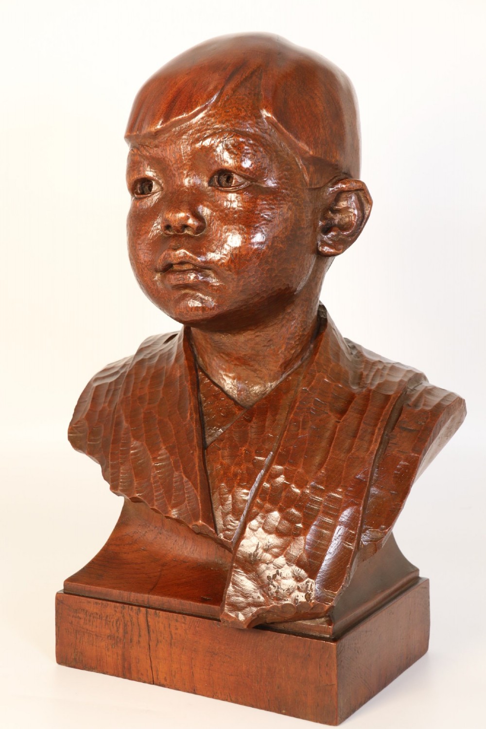 A carved walnut sculpture bust of a young child set upon a matching rectangular wooden plinth. View X