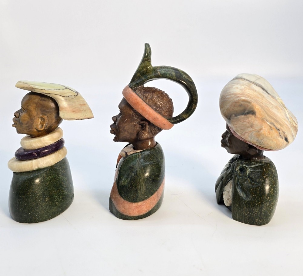 A trio of hand-carved African portrait busts crafted from multi-coloured polished stone depicting figures with distinctive headwear and detailed neck rings. View II