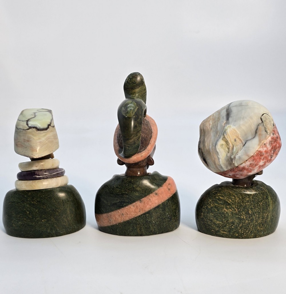 A trio of hand-carved African portrait busts crafted from multi-coloured polished stone depicting figures with distinctive headwear and detailed neck rings. View III