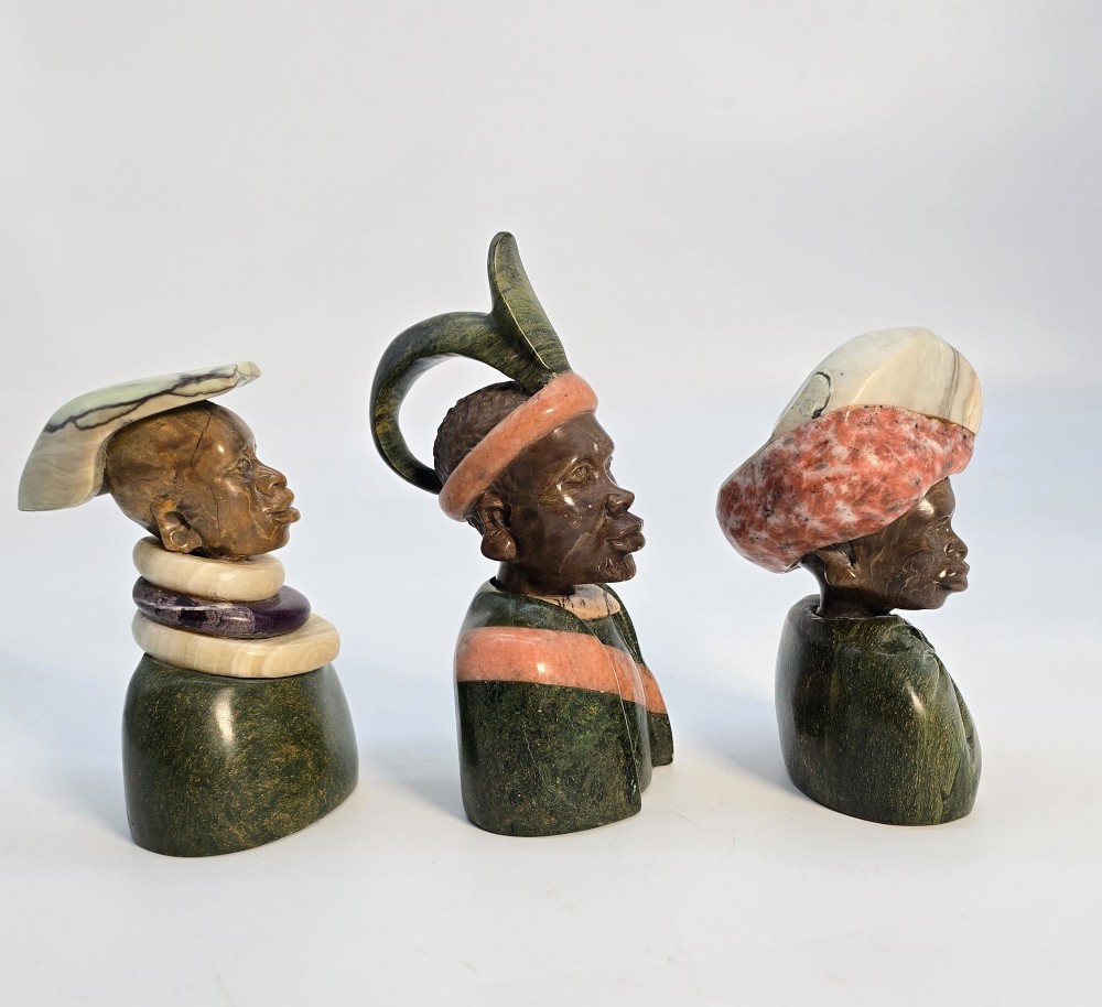A trio of hand-carved African portrait busts crafted from multi-coloured polished stone depicting figures with distinctive headwear and detailed neck rings. View IV
