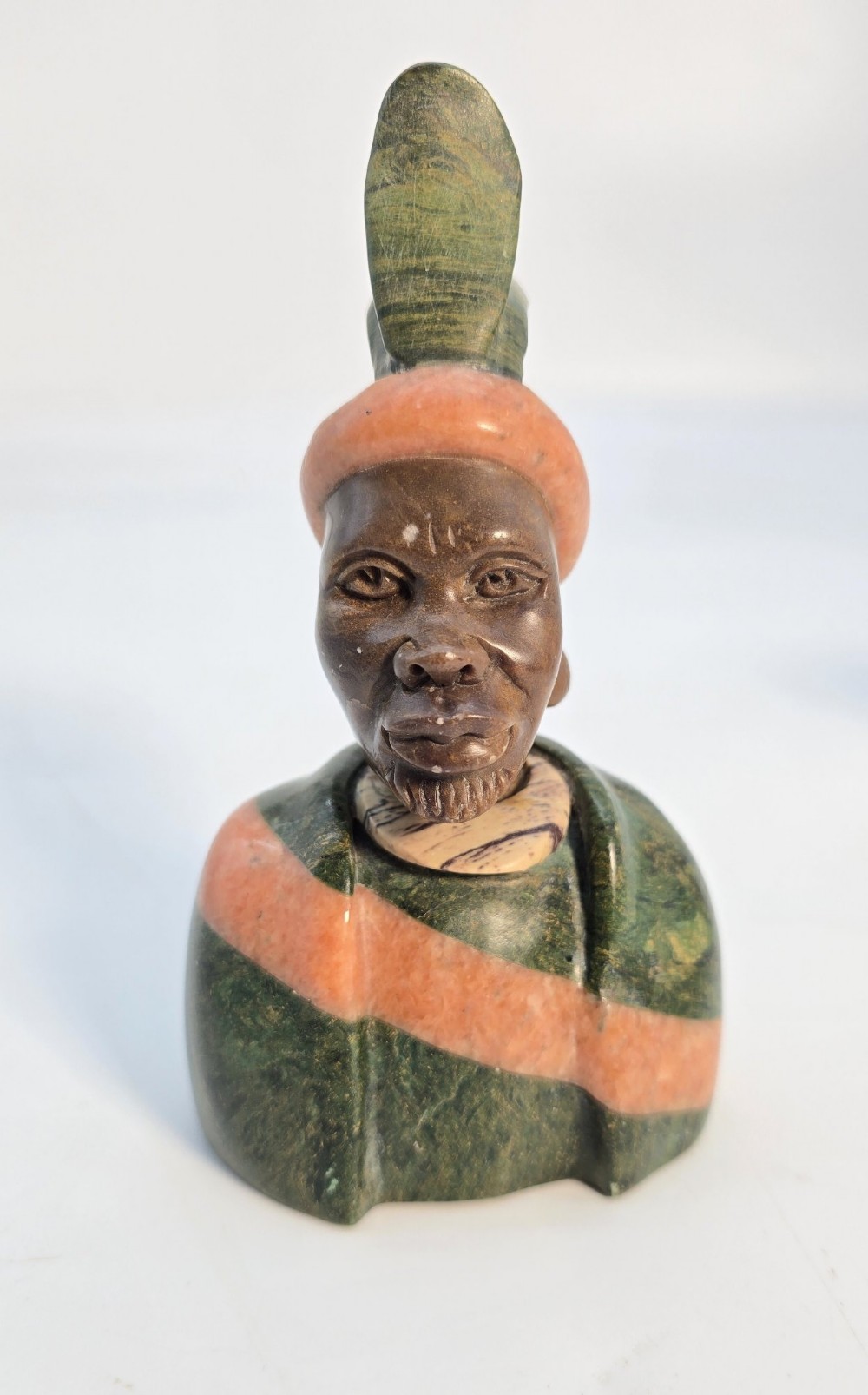 A trio of hand-carved African portrait busts crafted from multi-coloured polished stone depicting figures with distinctive headwear and detailed neck rings. View V