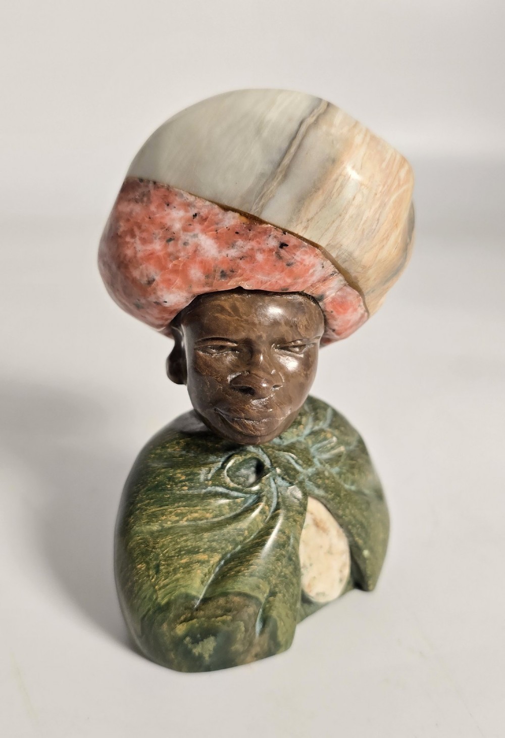 A trio of hand-carved African portrait busts crafted from multi-coloured polished stone depicting figures with distinctive headwear and detailed neck rings. View VI