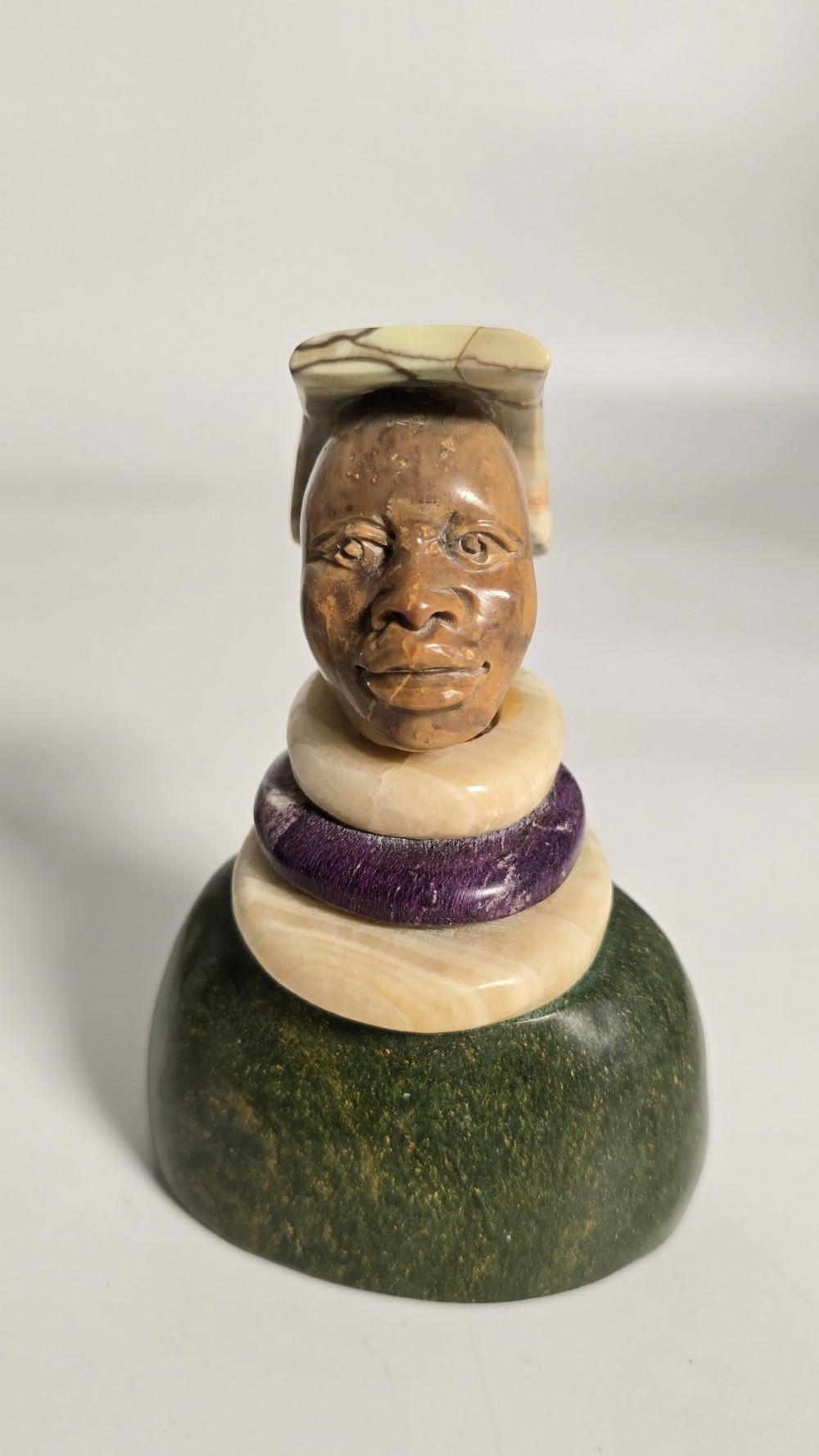 A trio of hand-carved African portrait busts crafted from multi-coloured polished stone depicting figures with distinctive headwear and detailed neck rings. View VII
