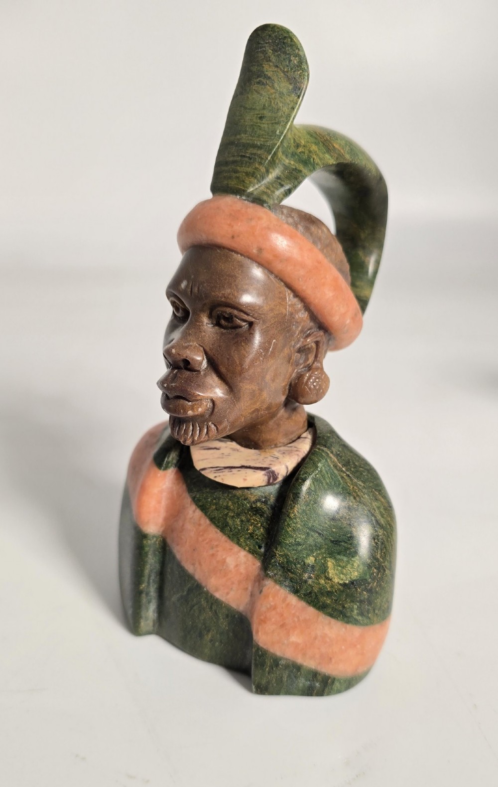 A trio of hand-carved African portrait busts crafted from multi-coloured polished stone depicting figures with distinctive headwear and detailed neck rings. View XI
