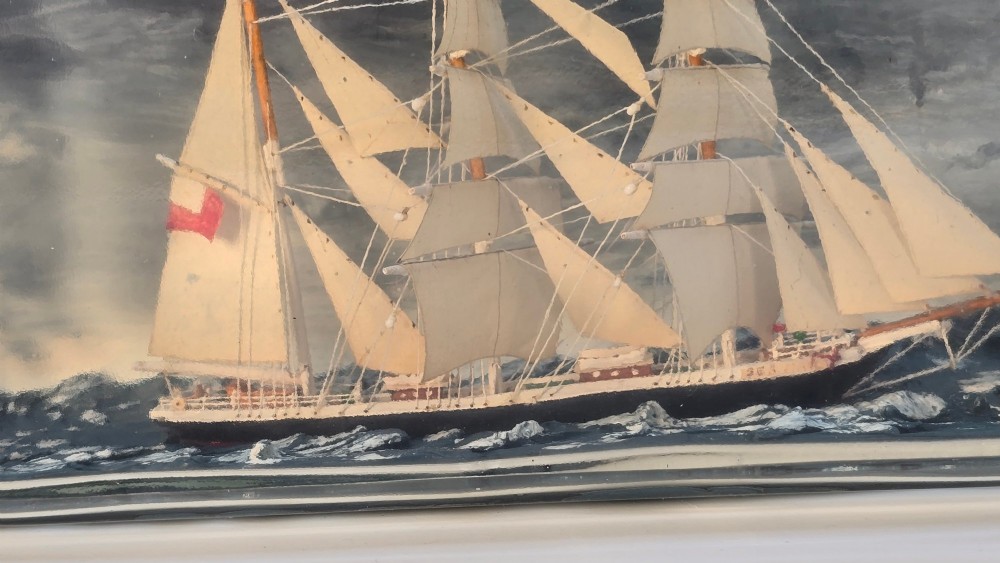 A horizontal clear glass bottle containing a detailed miniature three-masted sailing ship diorama set upon painted blue ocean waves with a rope-bound neck stopper. View VIII
