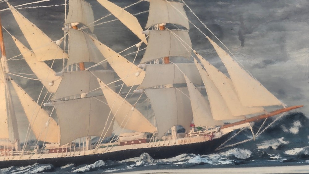 A horizontal clear glass bottle containing a detailed miniature three-masted sailing ship diorama set upon painted blue ocean waves with a rope-bound neck stopper. View IX