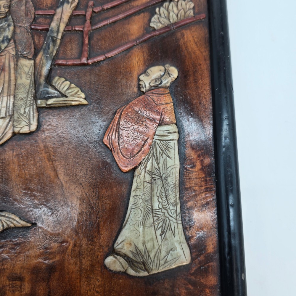 A vertical rectangular dark wood panel displaying a carved multi-coloured hardstone relief scene of figures beneath a tree and architectural structure. View VI