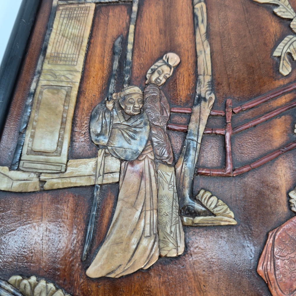 A vertical rectangular dark wood panel displaying a carved multi-coloured hardstone relief scene of figures beneath a tree and architectural structure. View VII