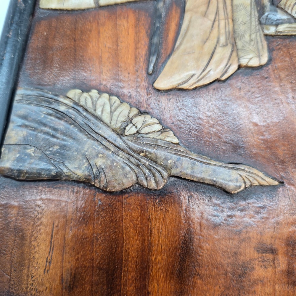 A vertical rectangular dark wood panel displaying a carved multi-coloured hardstone relief scene of figures beneath a tree and architectural structure. View X