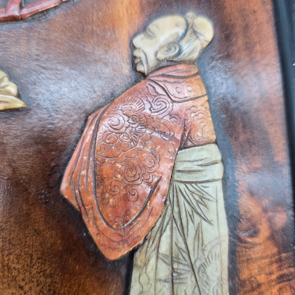 A vertical rectangular dark wood panel displaying a carved multi-coloured hardstone relief scene of figures beneath a tree and architectural structure. View XI