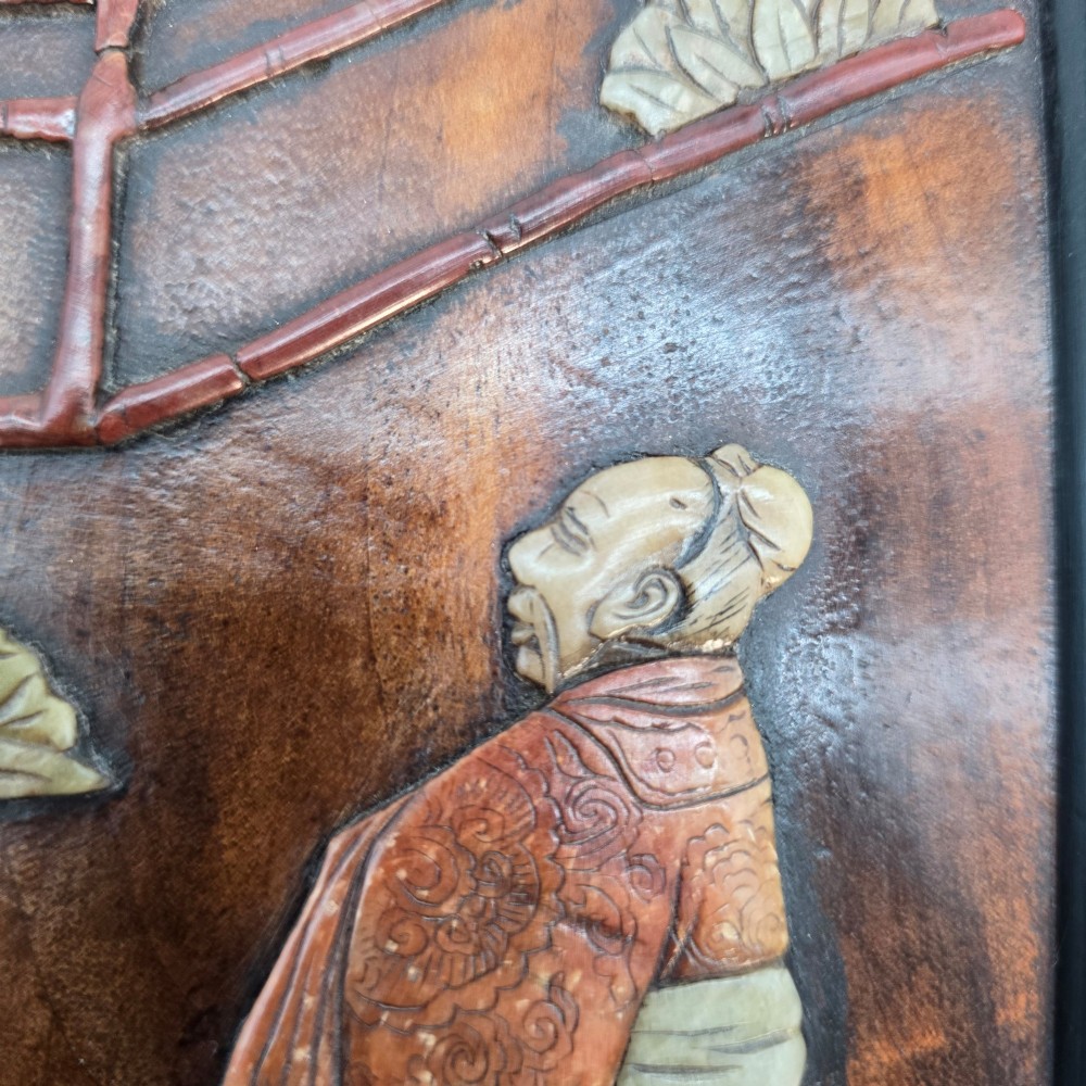 A vertical rectangular dark wood panel displaying a carved multi-coloured hardstone relief scene of figures beneath a tree and architectural structure. View XII