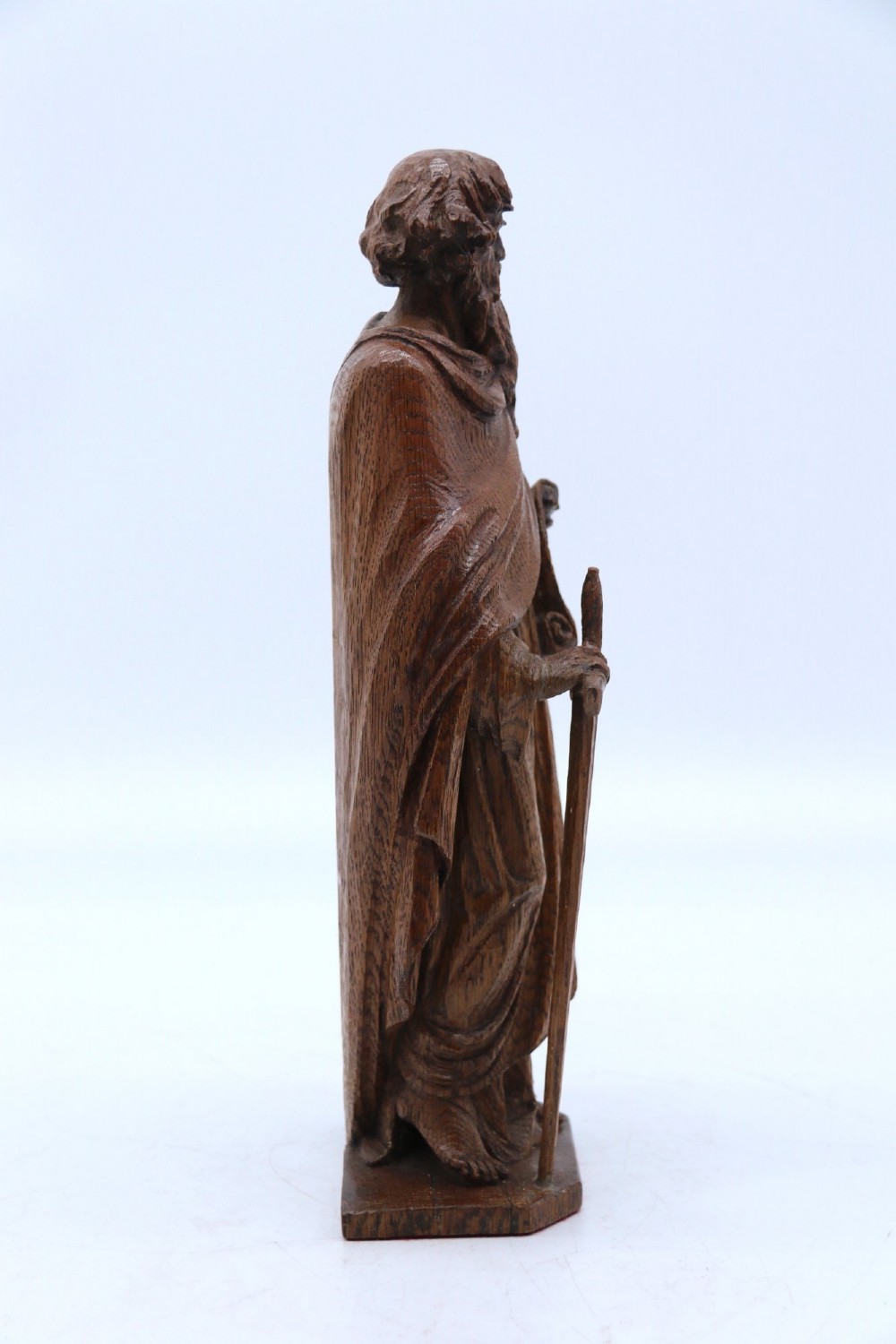 A carved oak wooden statue depicting Saint Paul holding a sword and scroll, standing on an octagonal wooden base. View V