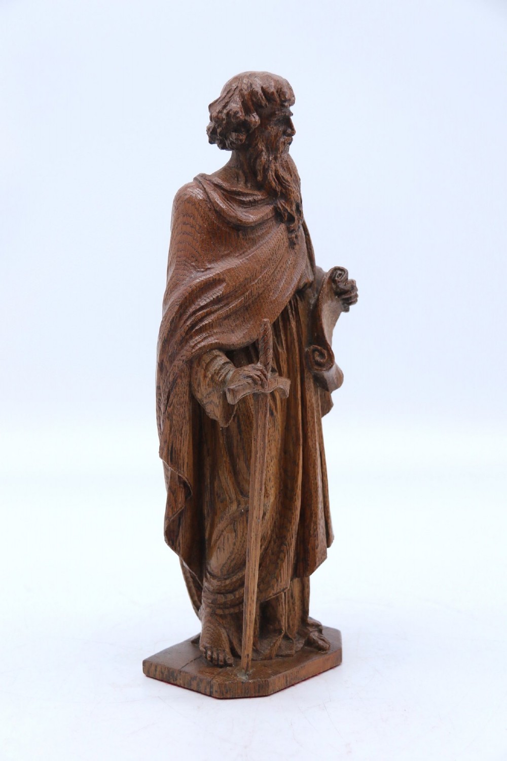 A carved oak wooden statue depicting Saint Paul holding a sword and scroll, standing on an octagonal wooden base. View VI