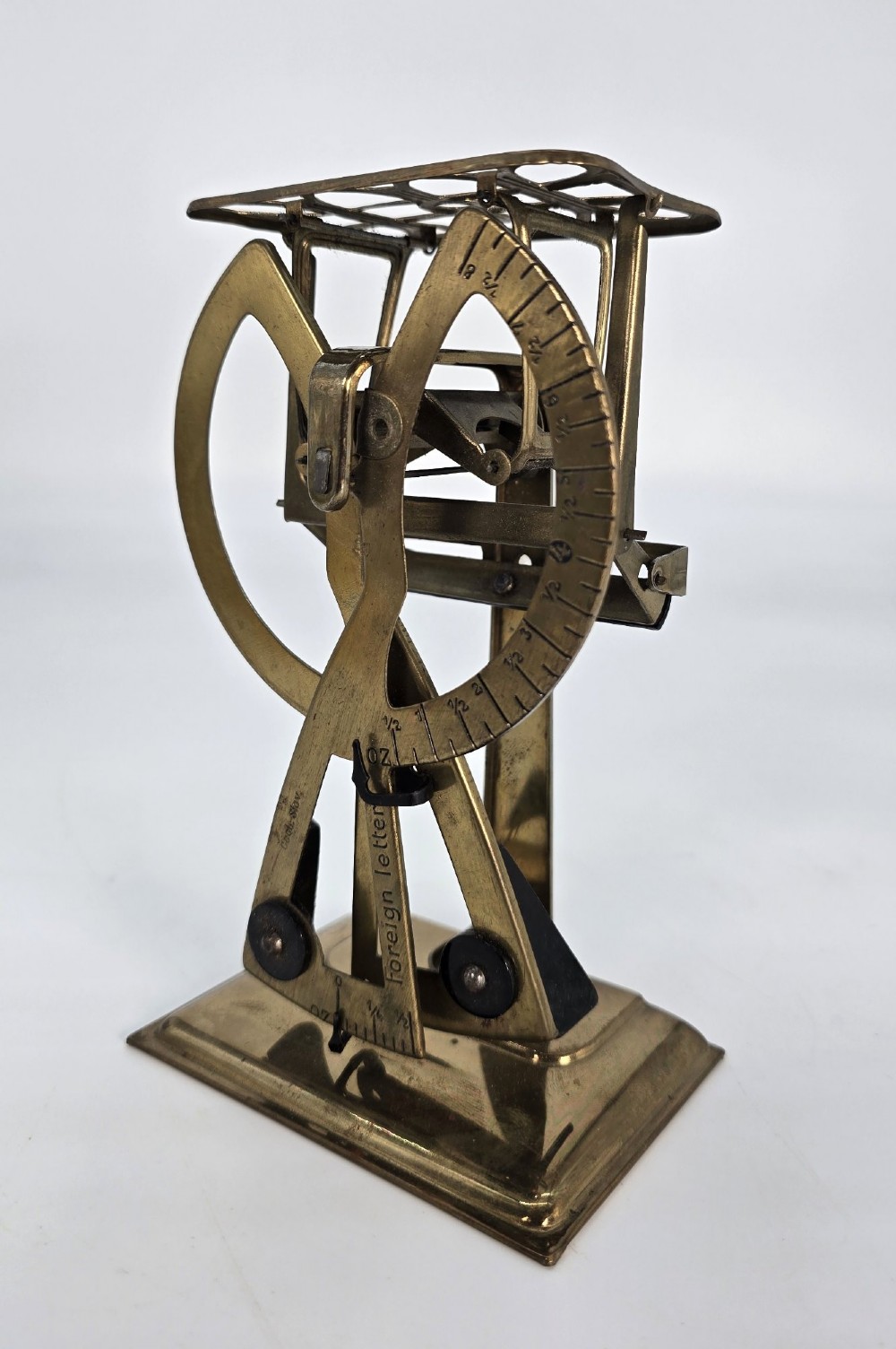 An Edwardian brass postal scale with an engraved curved measurement arc resting on a moulded rectangular base.
