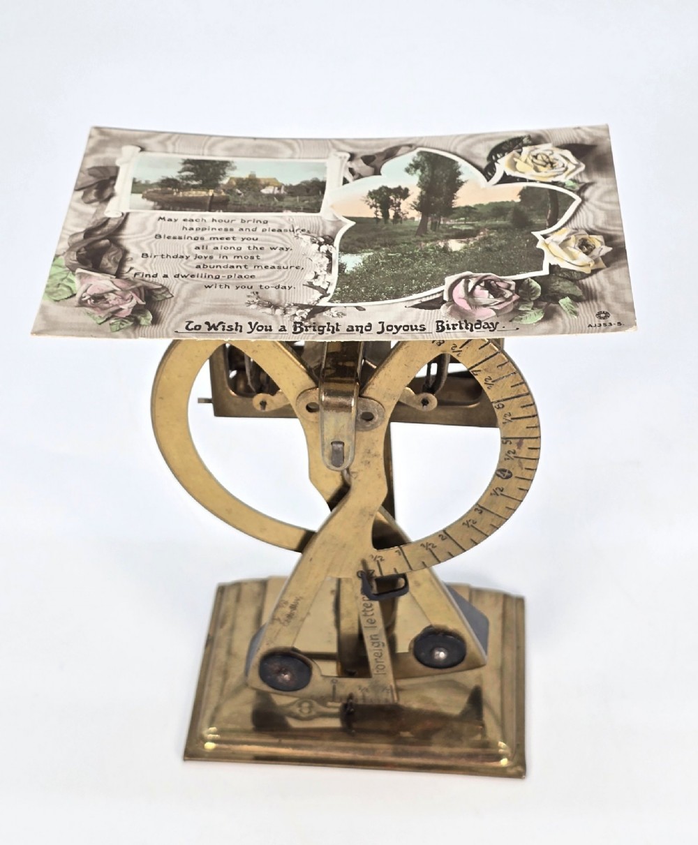 An Edwardian brass postal scale with an engraved curved measurement arc resting on a moulded rectangular base. View X