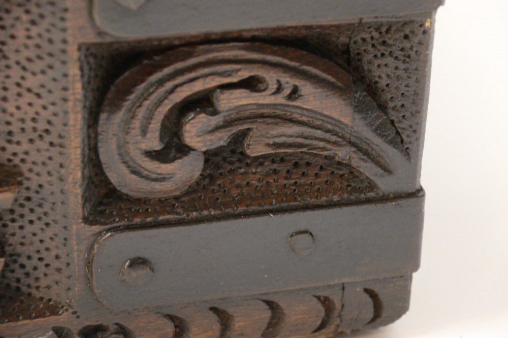 A dark carved oak strong box featuring metal binding straps, side drop handles, and relief carvings of figures and foliage. View VI