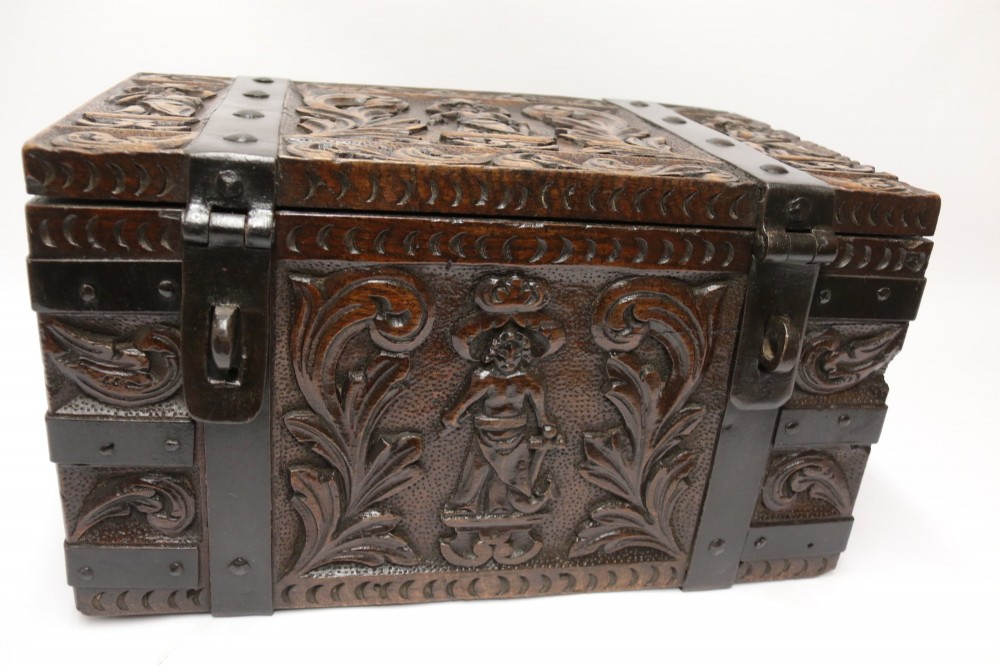 A dark carved oak strong box featuring metal binding straps, side drop handles, and relief carvings of figures and foliage. View VIII