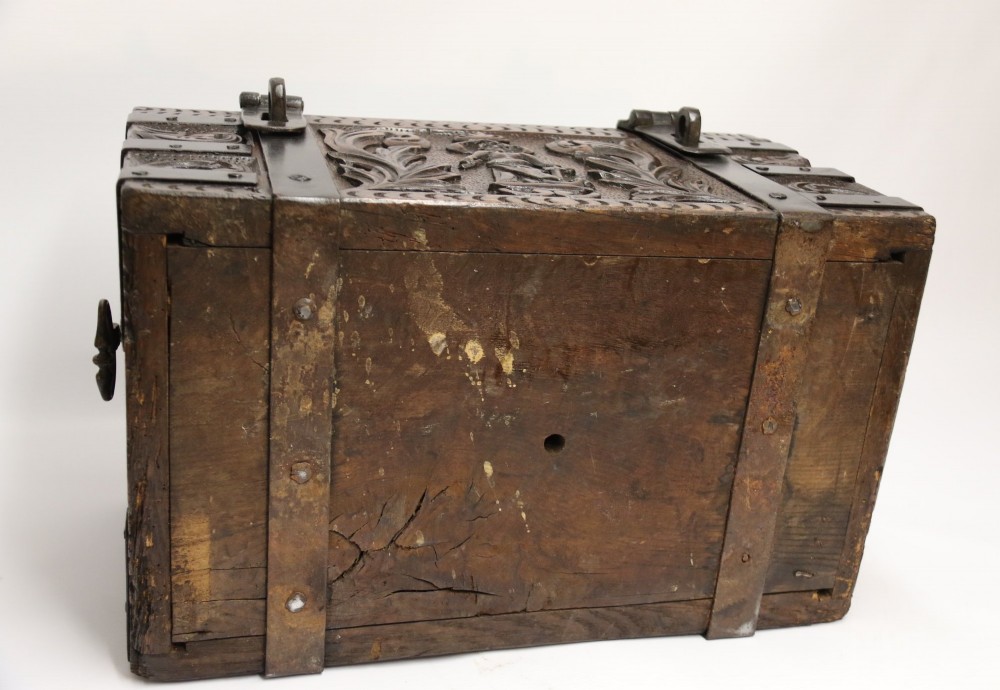 A dark carved oak strong box featuring metal binding straps, side drop handles, and relief carvings of figures and foliage. View XII