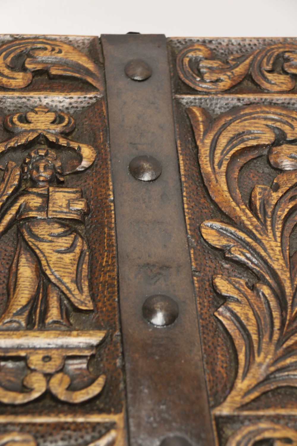 A dark carved oak strong box featuring metal binding straps, side drop handles, and relief carvings of figures and foliage. View XIV