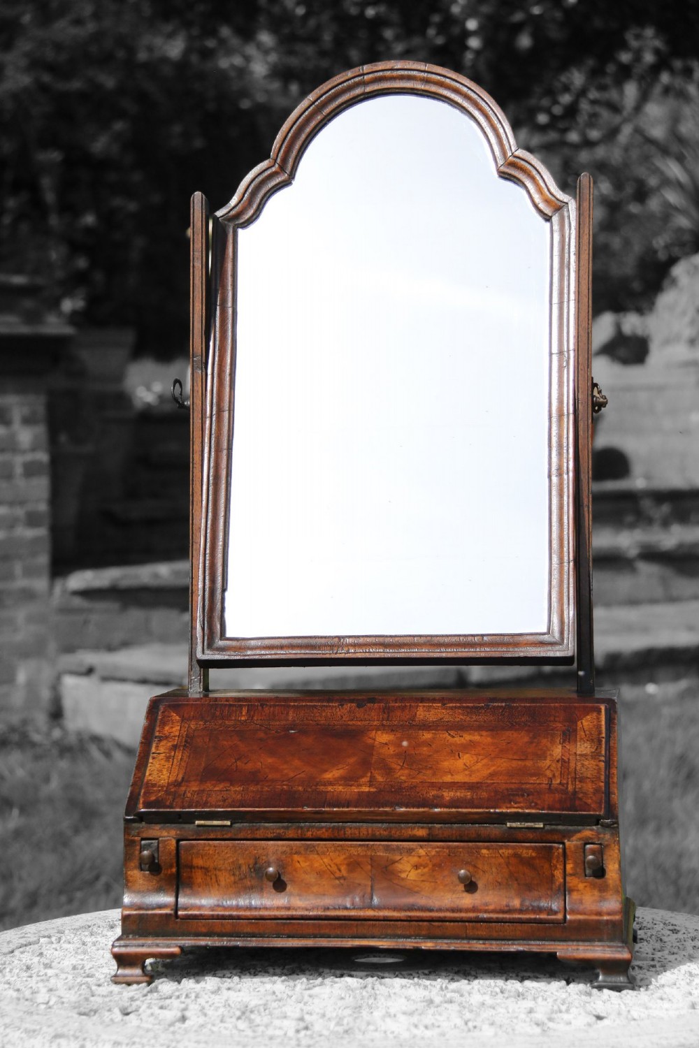 A Victorian figured walnut table mirror featuring an arched swivelling glass set above a slant-front miniature bureau base with a lower drawer.