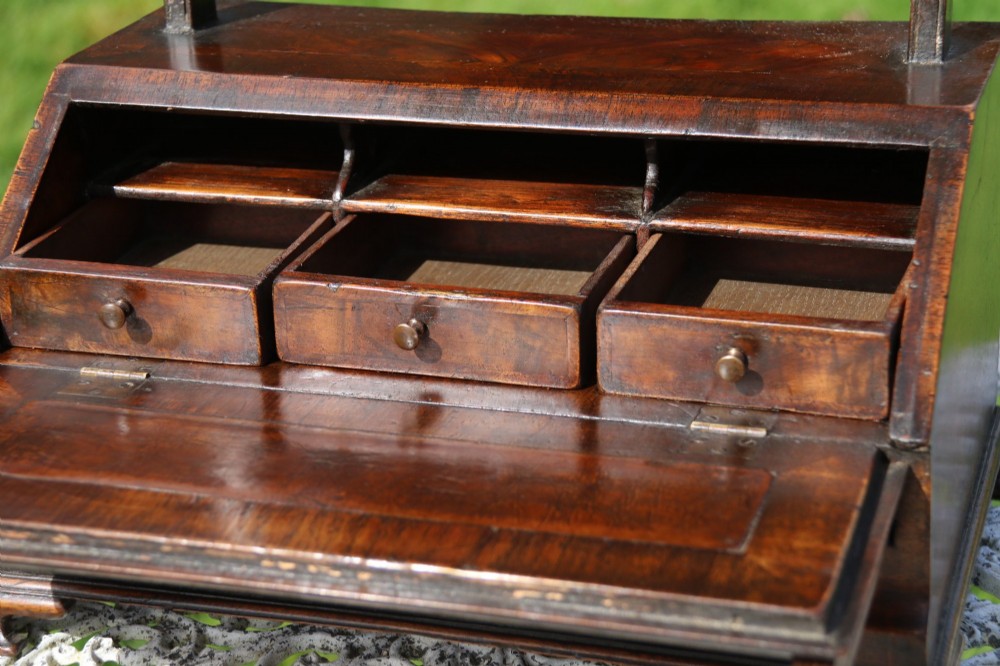 A Victorian figured walnut table mirror featuring an arched swivelling glass set above a slant-front miniature bureau base with a lower drawer. View V