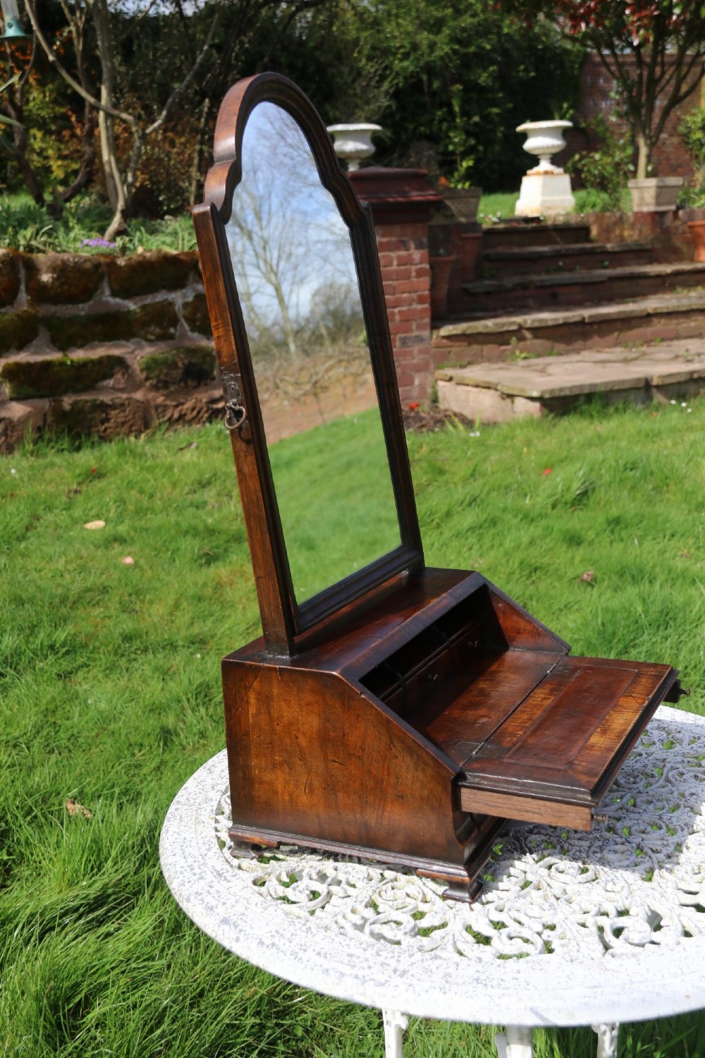 A Victorian figured walnut table mirror featuring an arched swivelling glass set above a slant-front miniature bureau base with a lower drawer. View VI