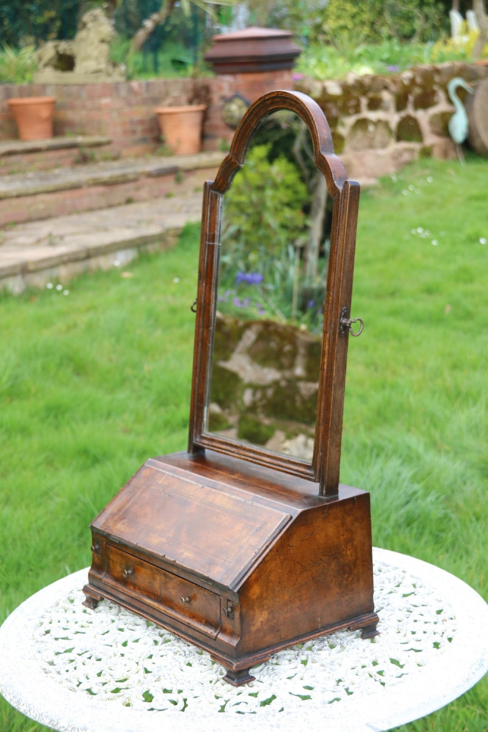 A Victorian figured walnut table mirror featuring an arched swivelling glass set above a slant-front miniature bureau base with a lower drawer. View XII
