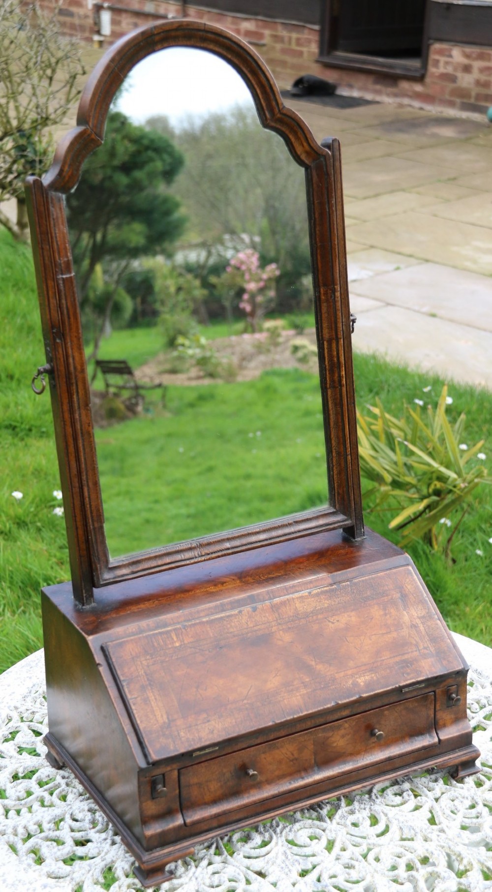 A Victorian figured walnut table mirror featuring an arched swivelling glass set above a slant-front miniature bureau base with a lower drawer. View XIII