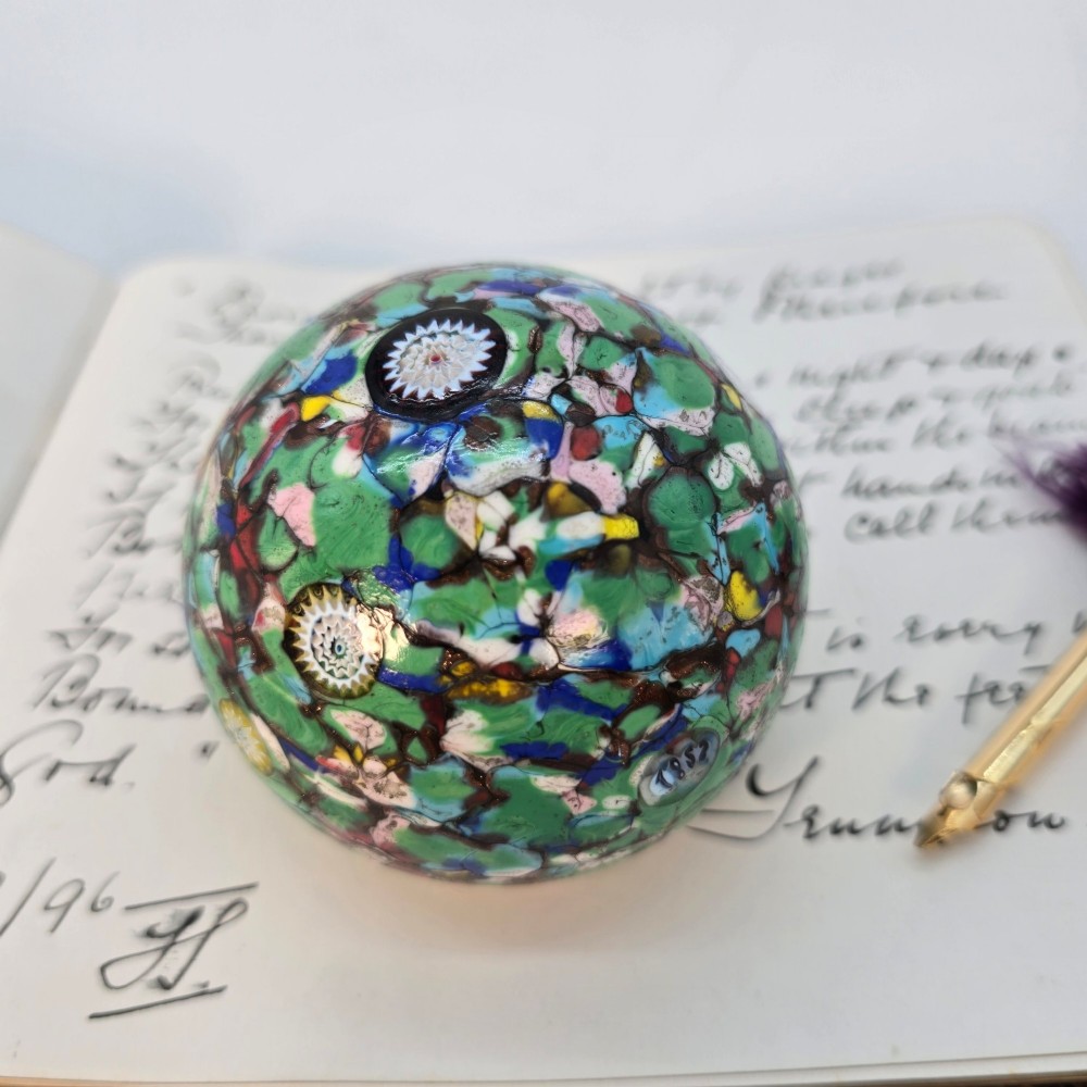 A spherical Murano glass paperweight featuring multicoloured millefiori cane patterns embedded within a vibrant green field.