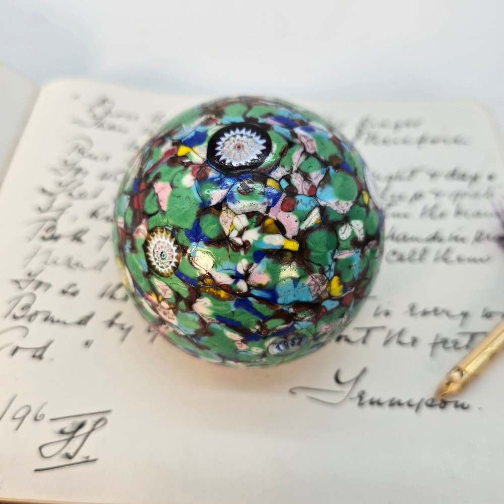 A spherical Murano glass paperweight featuring multicoloured millefiori cane patterns embedded within a vibrant green field. View III