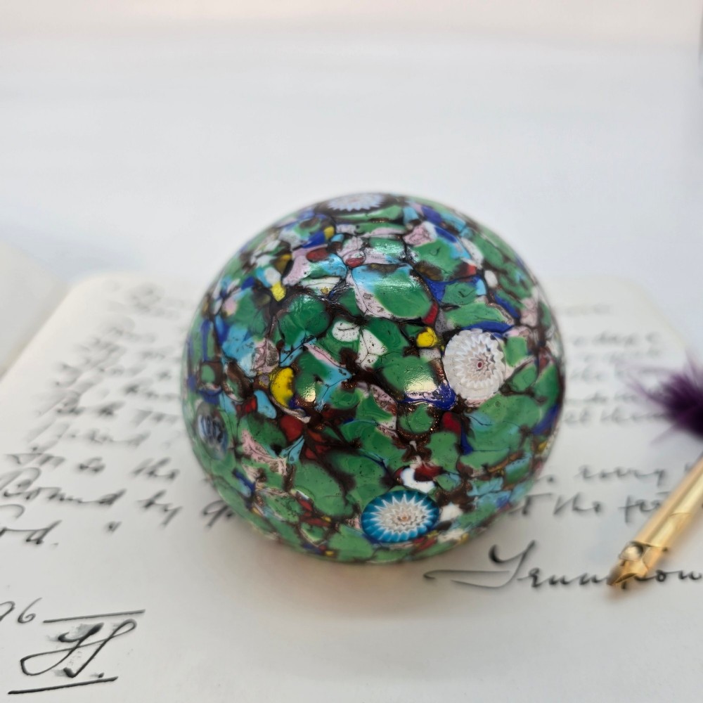 A spherical Murano glass paperweight featuring multicoloured millefiori cane patterns embedded within a vibrant green field. View V