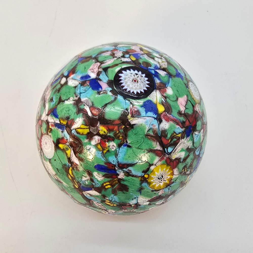 A spherical Murano glass paperweight featuring multicoloured millefiori cane patterns embedded within a vibrant green field. View VI