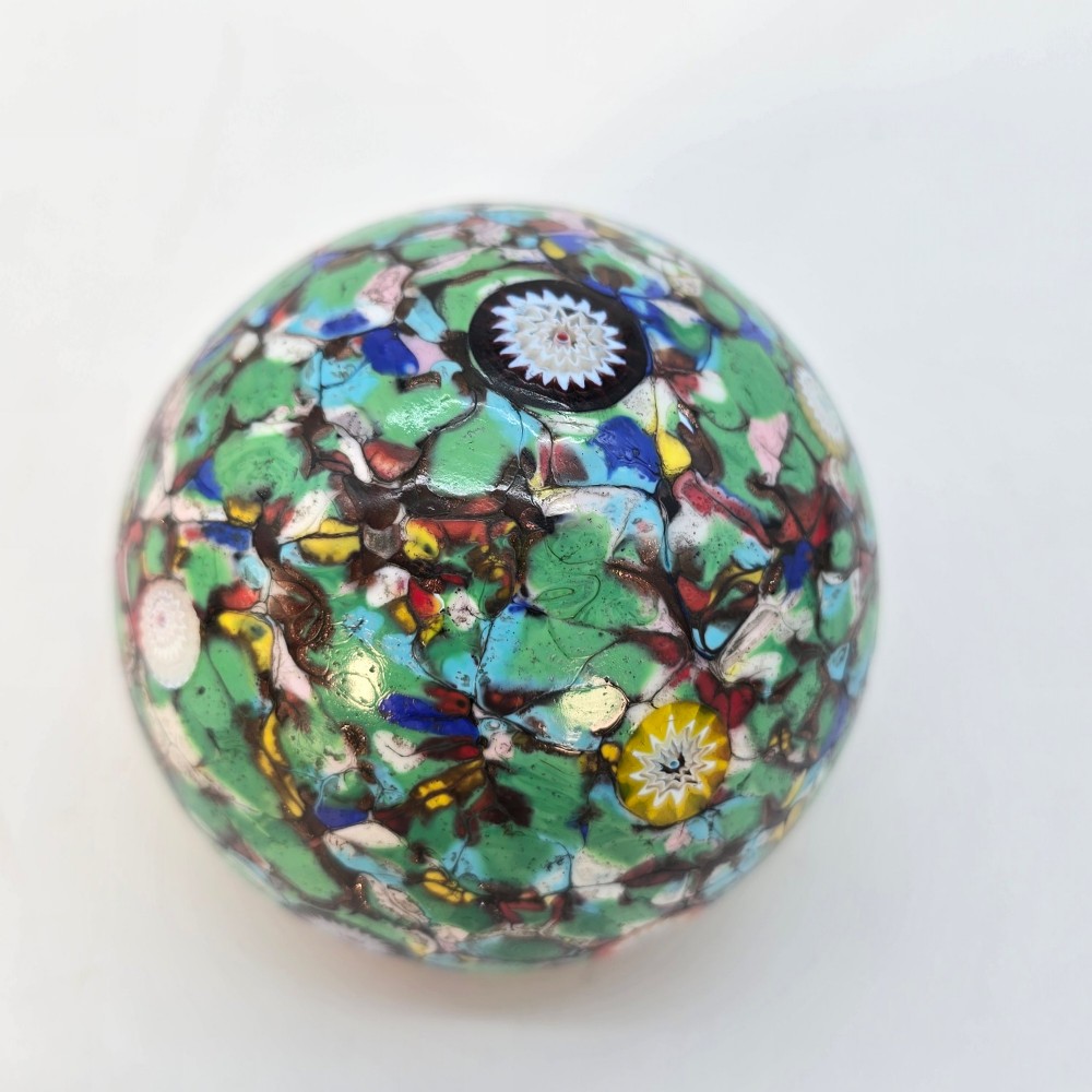 A spherical Murano glass paperweight featuring multicoloured millefiori cane patterns embedded within a vibrant green field. View VII