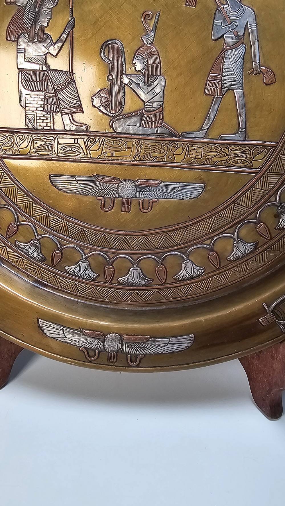 A circular brass charger featuring mixed silver and copper inlay artwork depicting Egyptian figures, cartouches, lotus flower borders, and winged sun disc motifs. View III