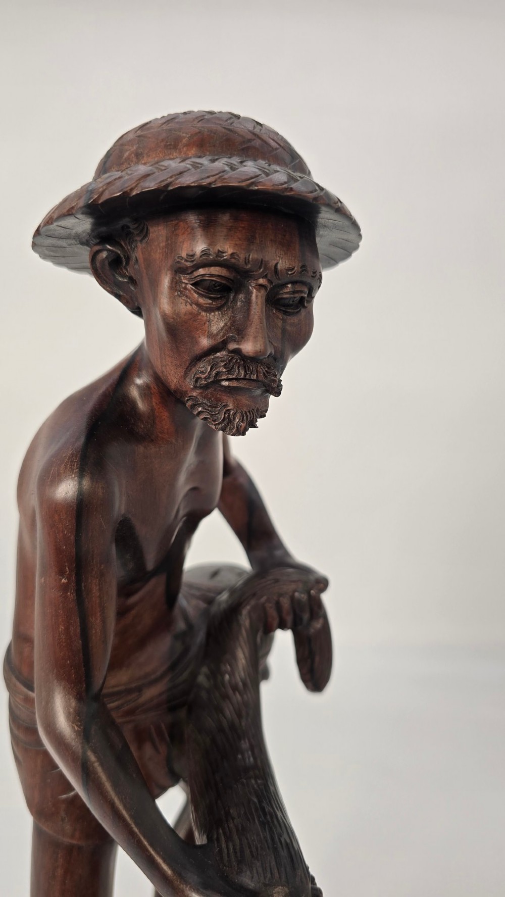 A hand-carved dark hardwood sculpture depicting a standing fisherman holding a woven net and basket, set on an organic carved base. View IV