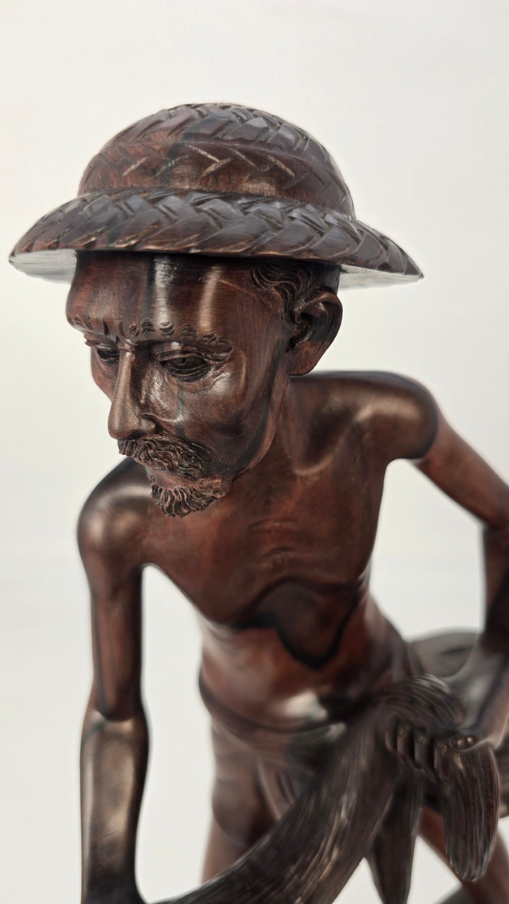 A hand-carved dark hardwood sculpture depicting a standing fisherman holding a woven net and basket, set on an organic carved base. View VII