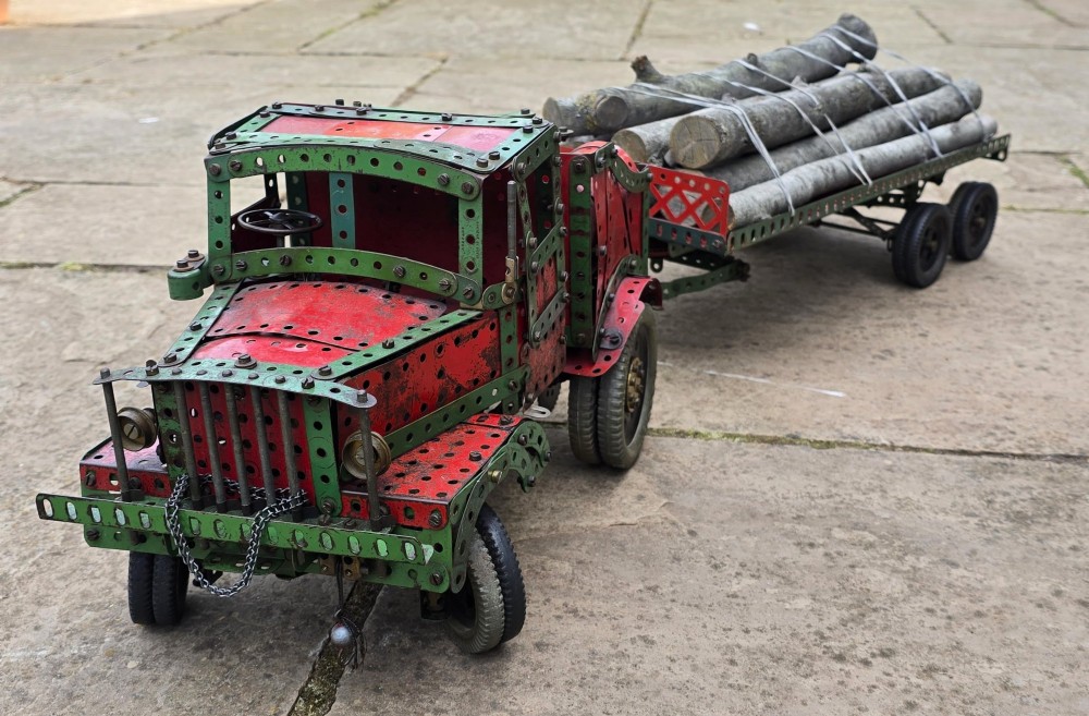 A detailed 1930s red and green Meccano model truck with a loaded timber trailer.