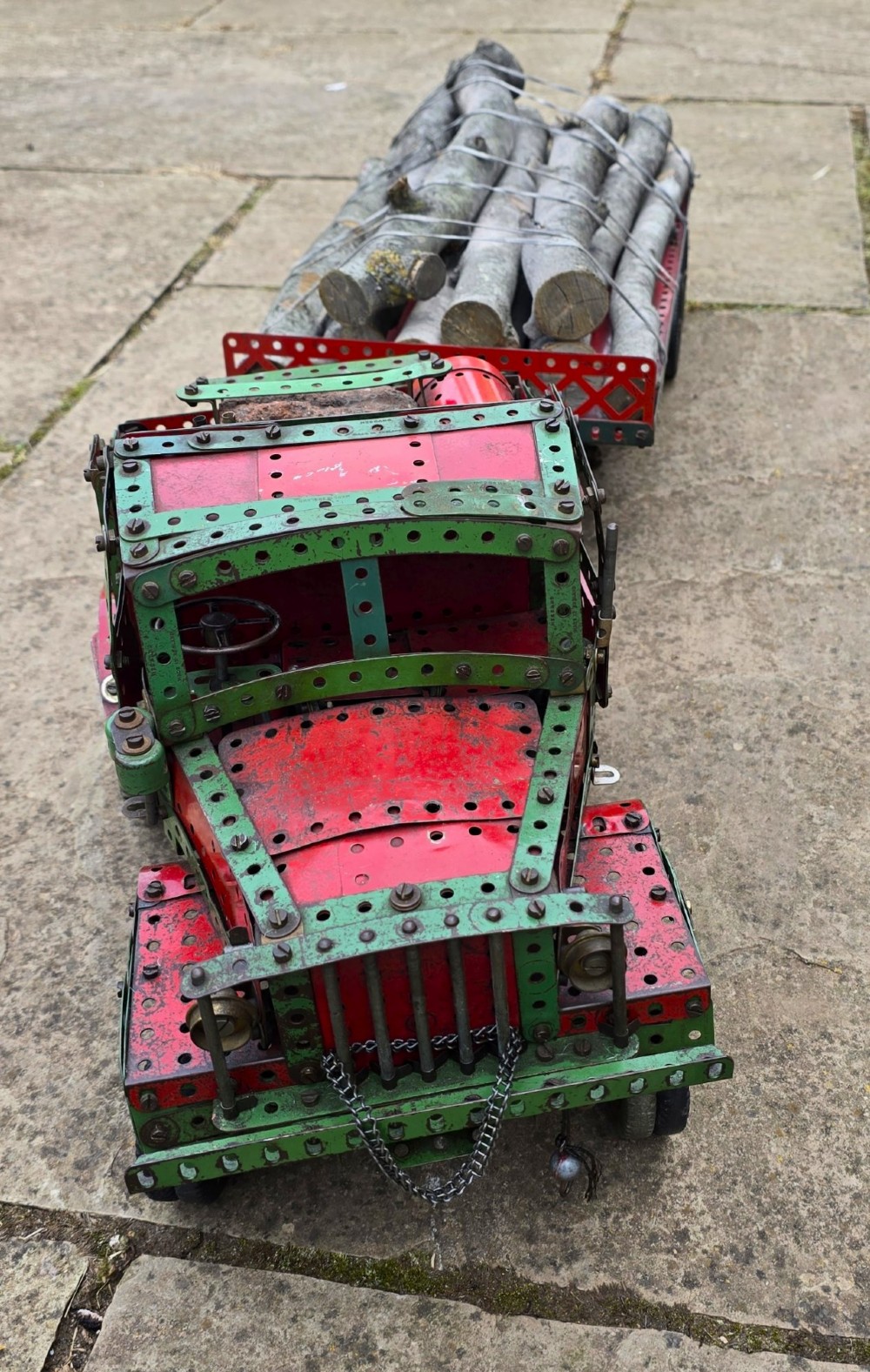 A detailed 1930s red and green Meccano model truck with a loaded timber trailer. View II