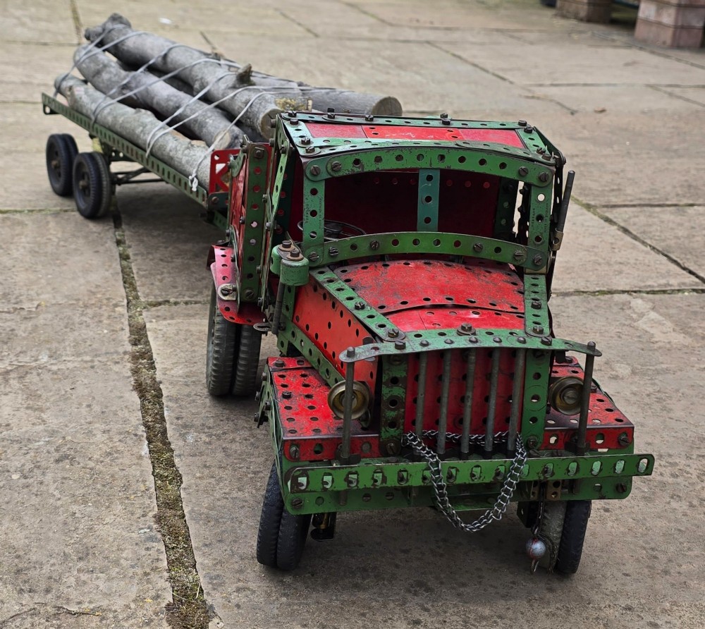 A detailed 1930s red and green Meccano model truck with a loaded timber trailer. View III