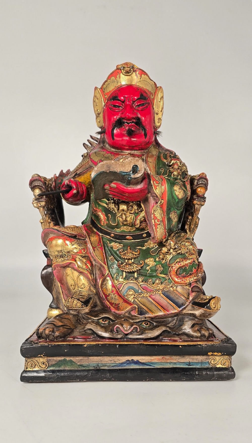 A carved Chinese lacquered wooden figure seated on a throne, rendered in bright red, green, and gold paint with intricate details.