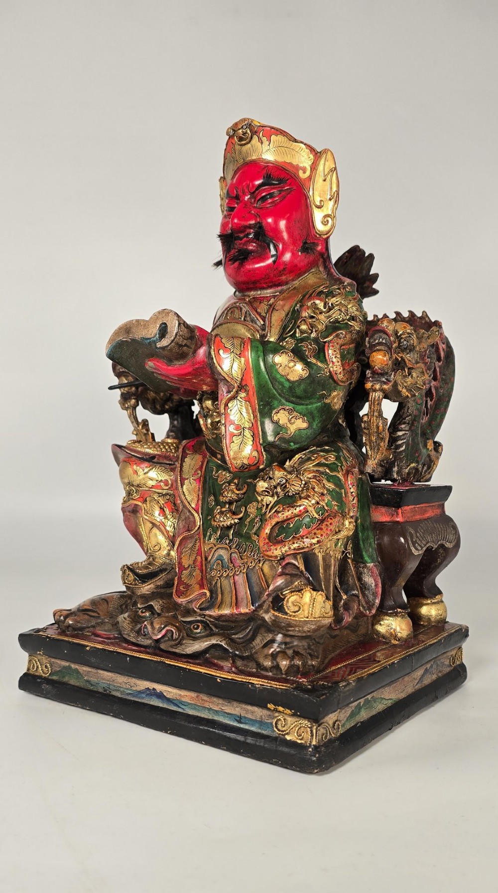 A carved Chinese lacquered wooden figure seated on a throne, rendered in bright red, green, and gold paint with intricate details. View II