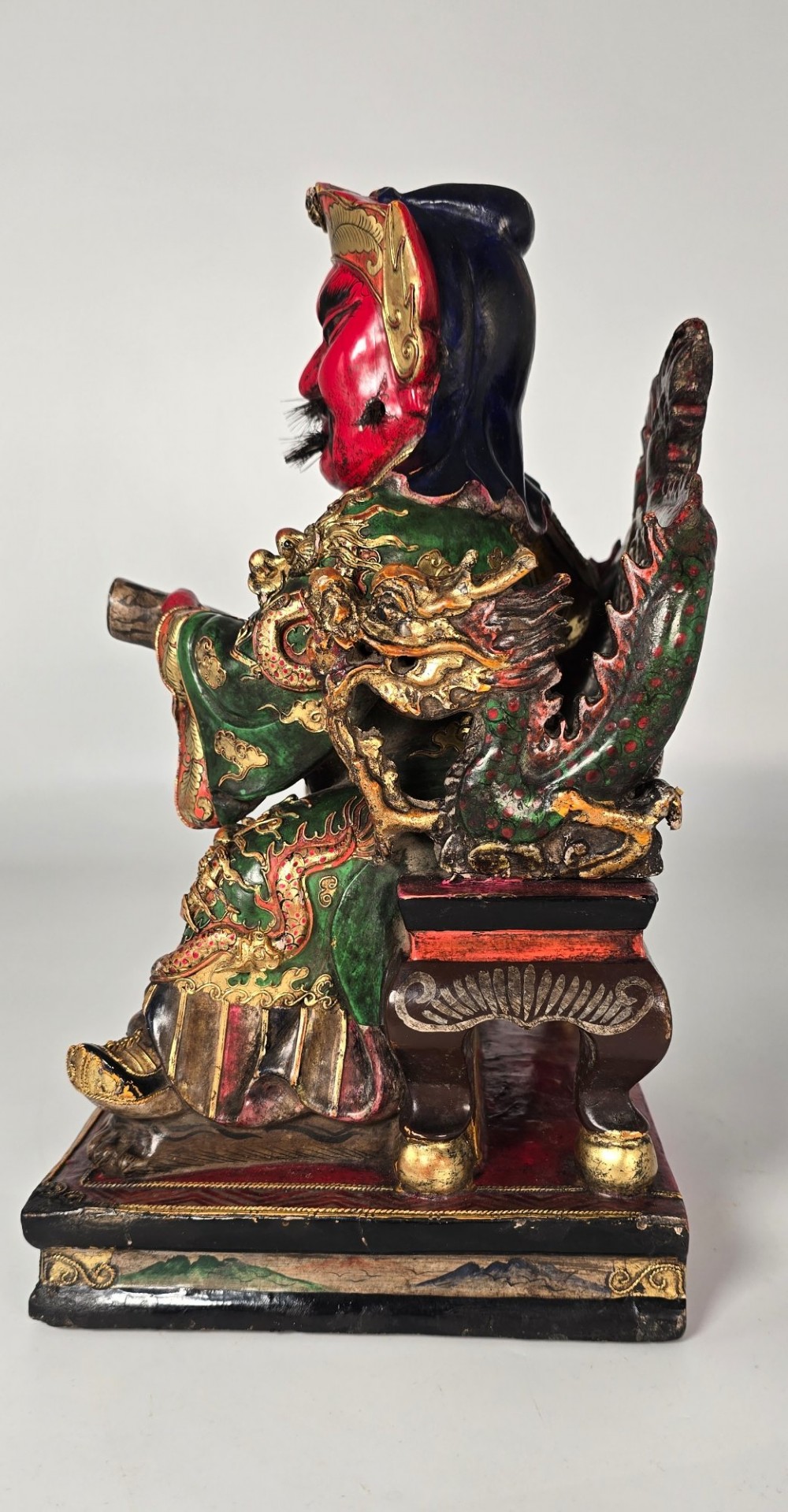 A carved Chinese lacquered wooden figure seated on a throne, rendered in bright red, green, and gold paint with intricate details. View III