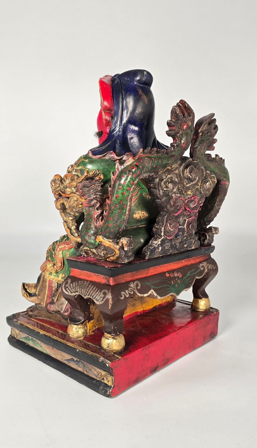 A carved Chinese lacquered wooden figure seated on a throne, rendered in bright red, green, and gold paint with intricate details. View IV