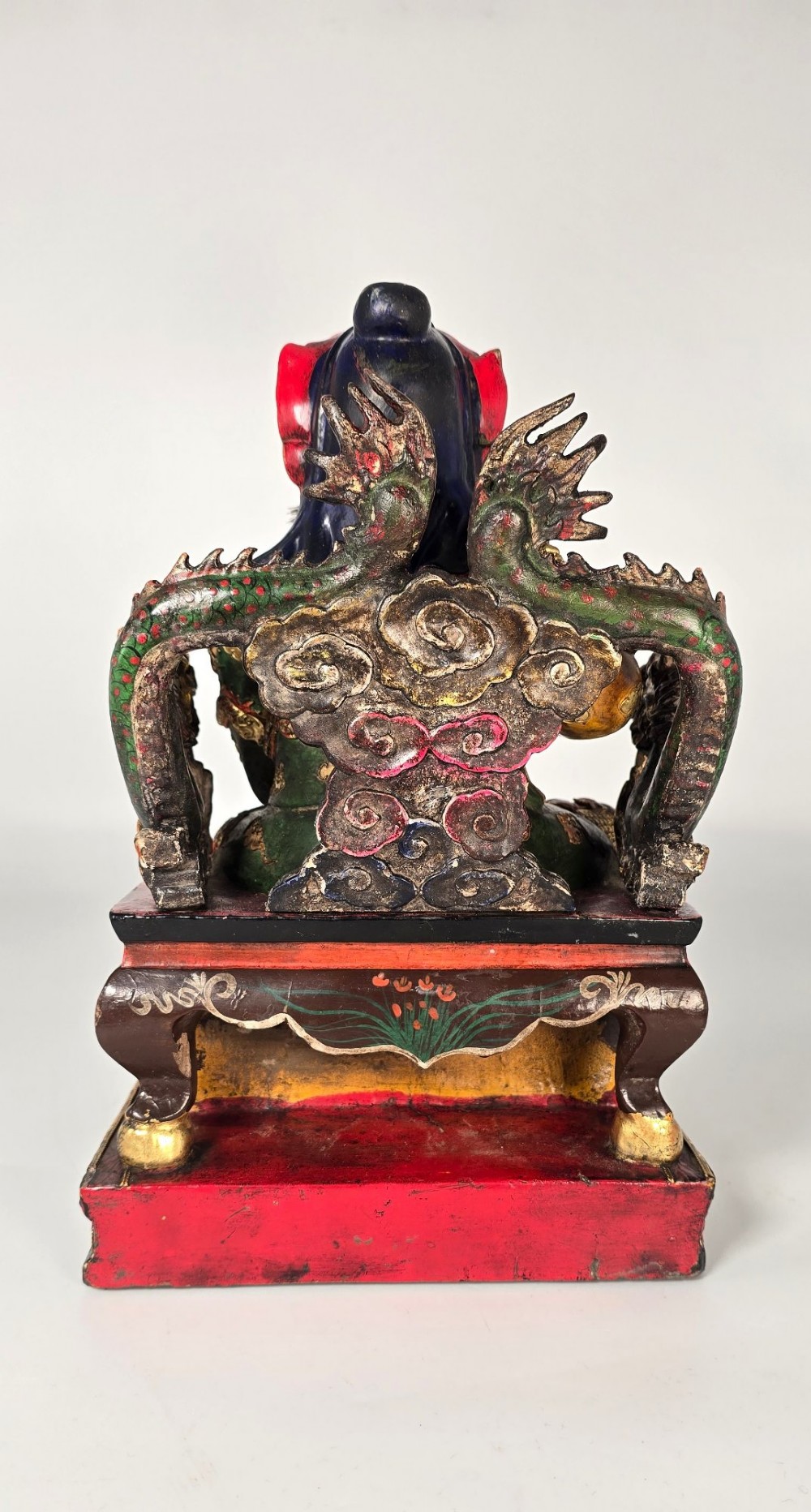 A carved Chinese lacquered wooden figure seated on a throne, rendered in bright red, green, and gold paint with intricate details. View V