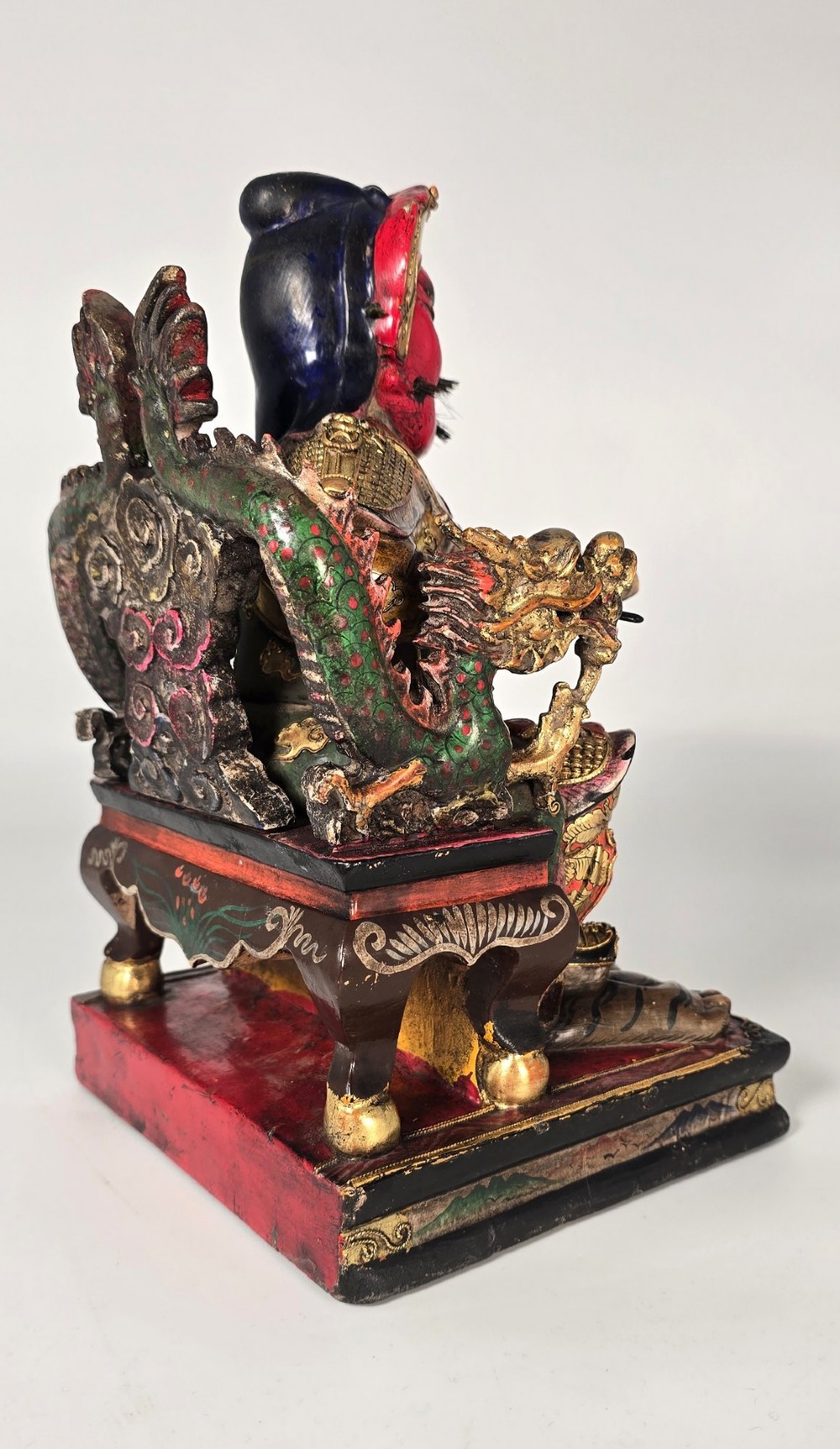 A carved Chinese lacquered wooden figure seated on a throne, rendered in bright red, green, and gold paint with intricate details. View VI