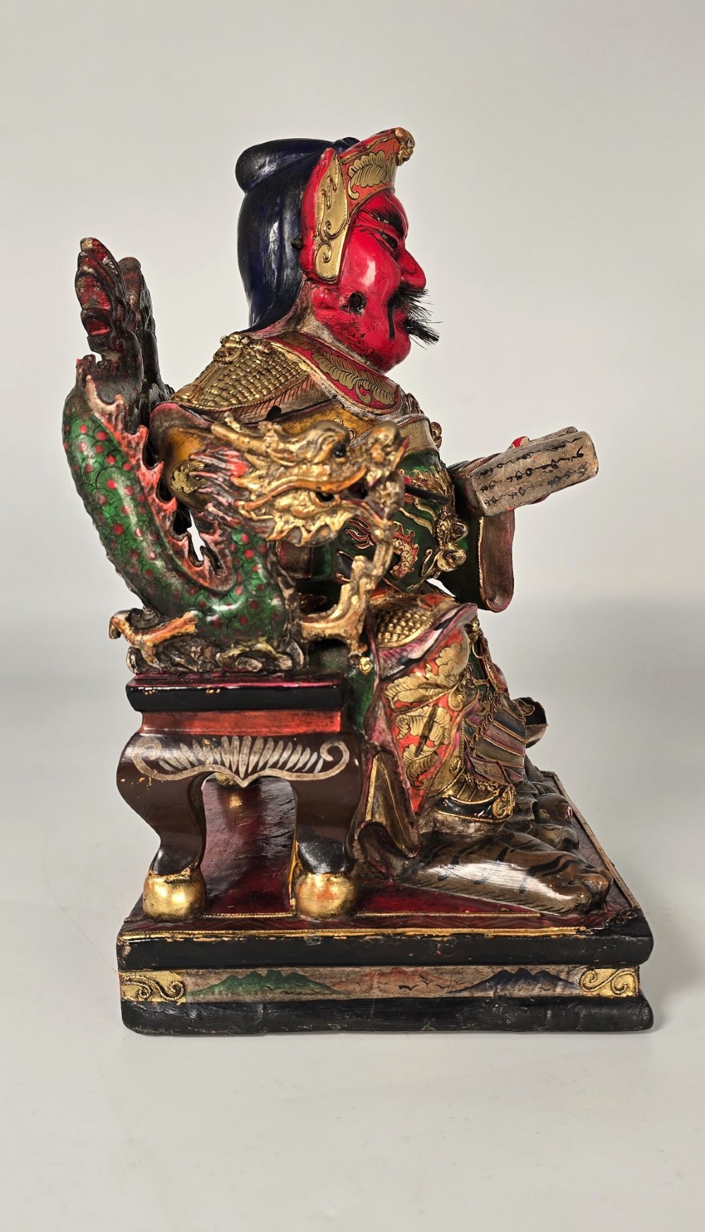 A carved Chinese lacquered wooden figure seated on a throne, rendered in bright red, green, and gold paint with intricate details. View VII