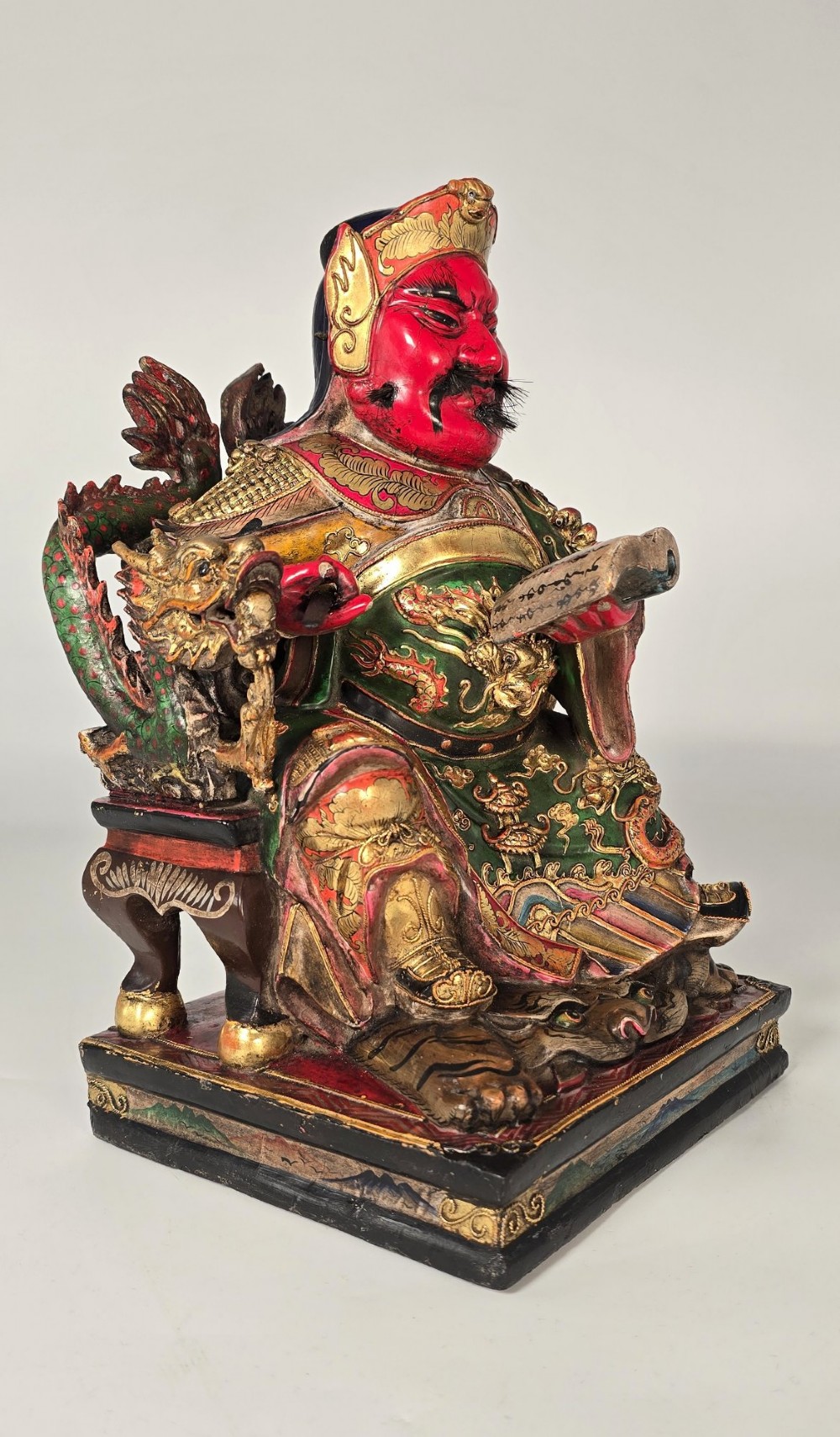 A carved Chinese lacquered wooden figure seated on a throne, rendered in bright red, green, and gold paint with intricate details. View VIII