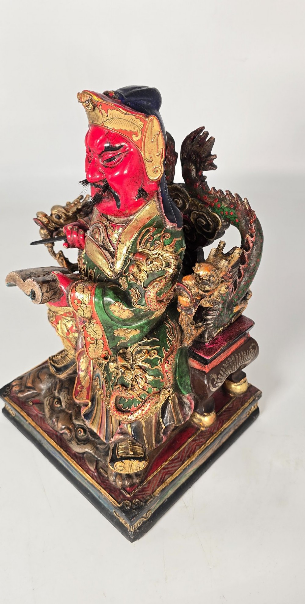 A carved Chinese lacquered wooden figure seated on a throne, rendered in bright red, green, and gold paint with intricate details. View IX