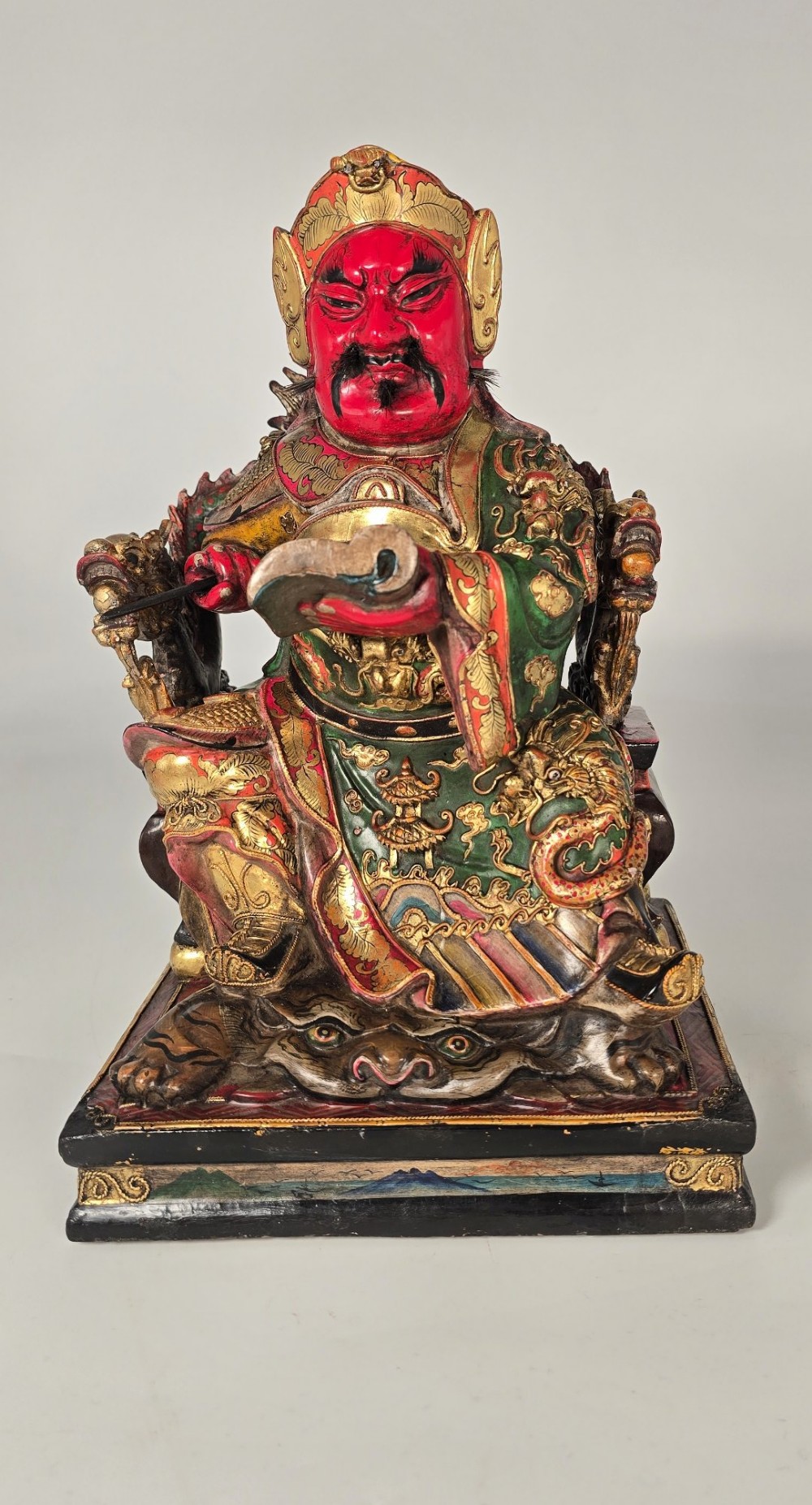A carved Chinese lacquered wooden figure seated on a throne, rendered in bright red, green, and gold paint with intricate details. View XIII