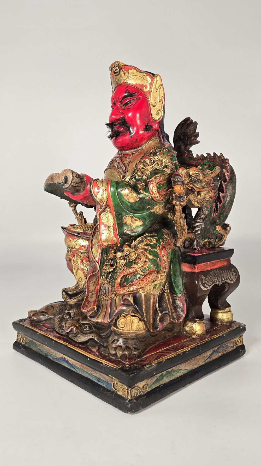 A carved Chinese lacquered wooden figure seated on a throne, rendered in bright red, green, and gold paint with intricate details. View XIV